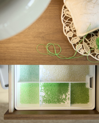 Top view of white KUGGIS insert with five compartments holding green pearls, inside a drawer with green yarn on top.