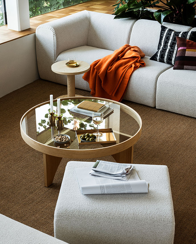 Una sala de estar con sofás de 4 plazas STOCKHOLM 2025 en color beige y pufs alrededor de una mesa de centro STOCKHOLM 2025 con acabado en roble y cristal.