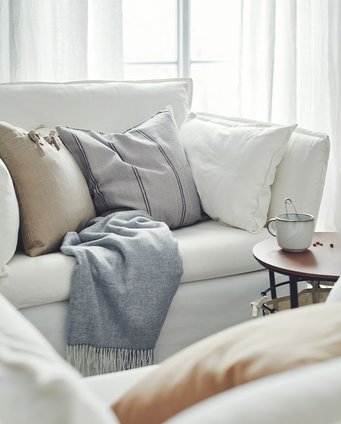 Una sala de estar con un sillón blanco BACKSÄLEN de un asiento y medio con cojines y una manta junto a una mesa auxiliar ÄNGESBYN.