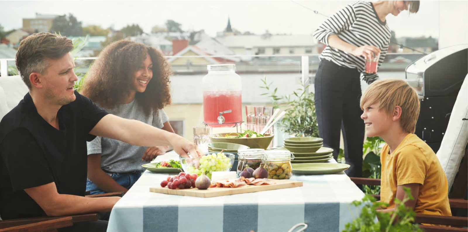 Personas compartiendo comida en una mesa exterior con bebidas y aperitivos.