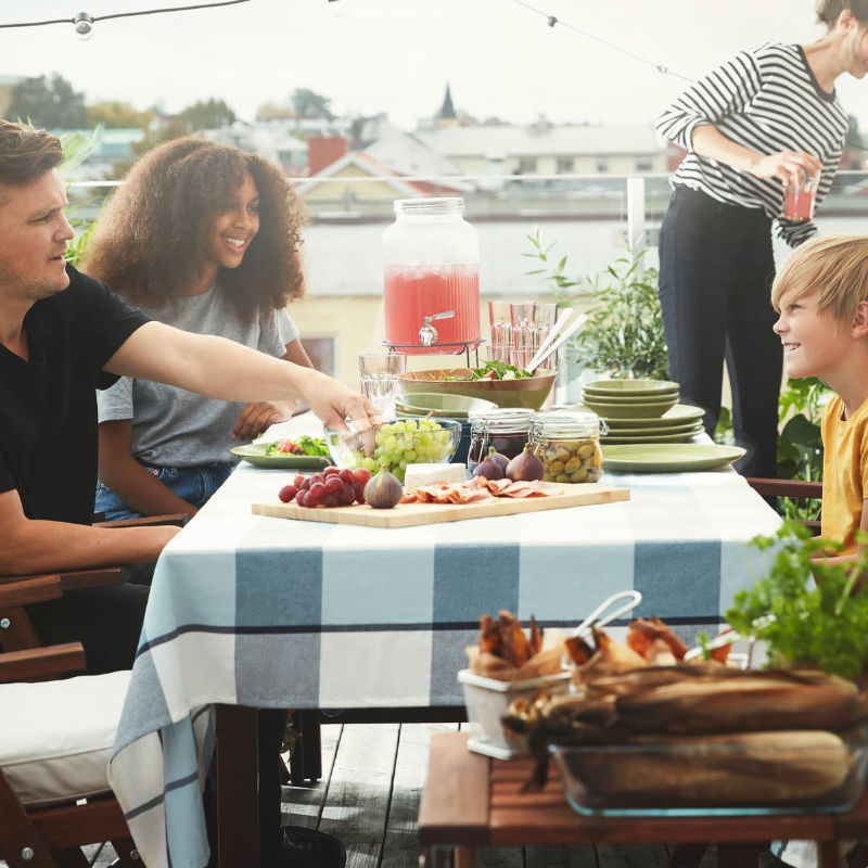 Personas compartiendo comida en una mesa exterior con bebidas y aperitivos.