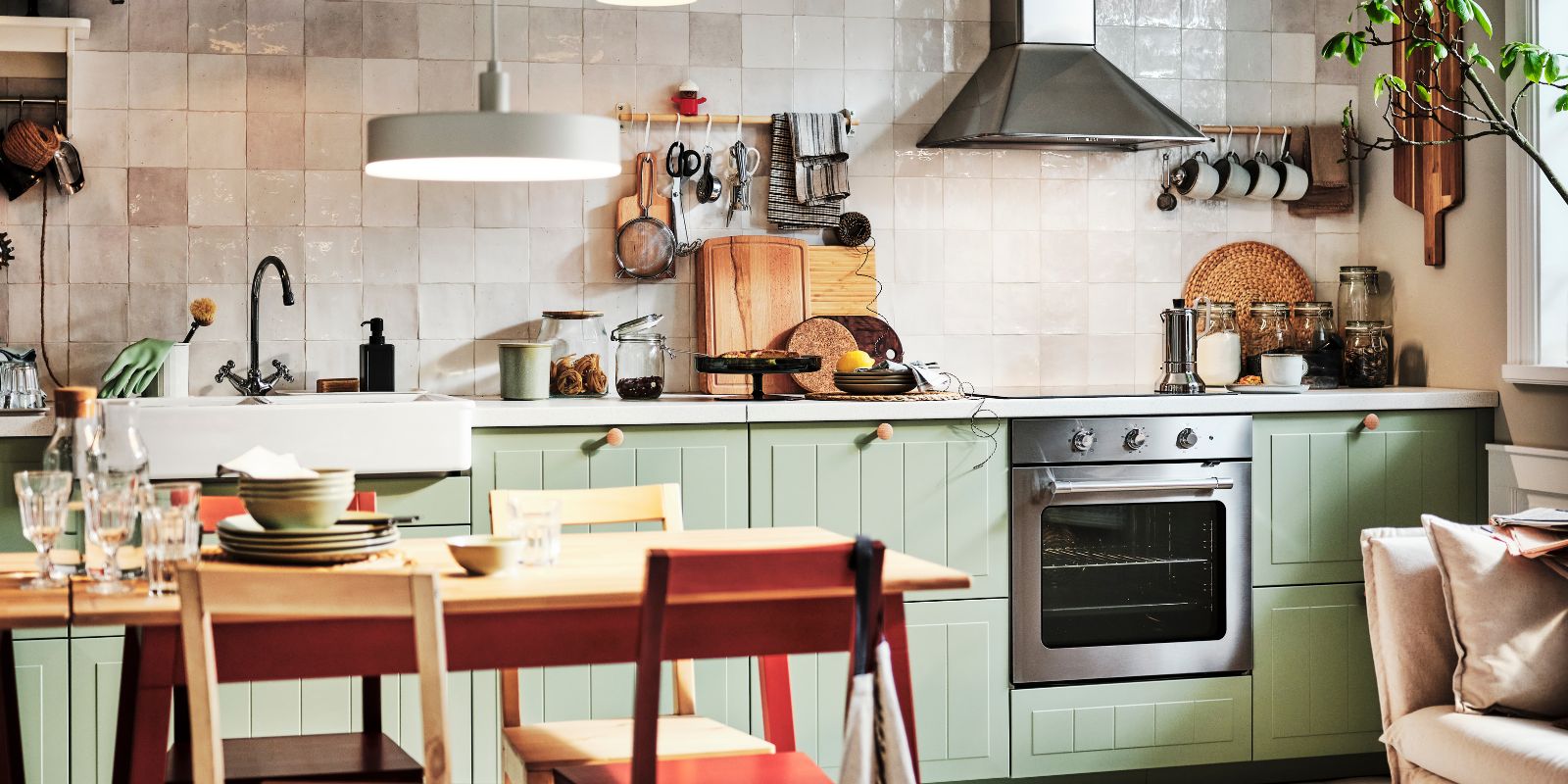 Kitchen with STENSUND green doors, tiled backsplash, stainless hood, and hanging utensils in a warm, rustic setup.