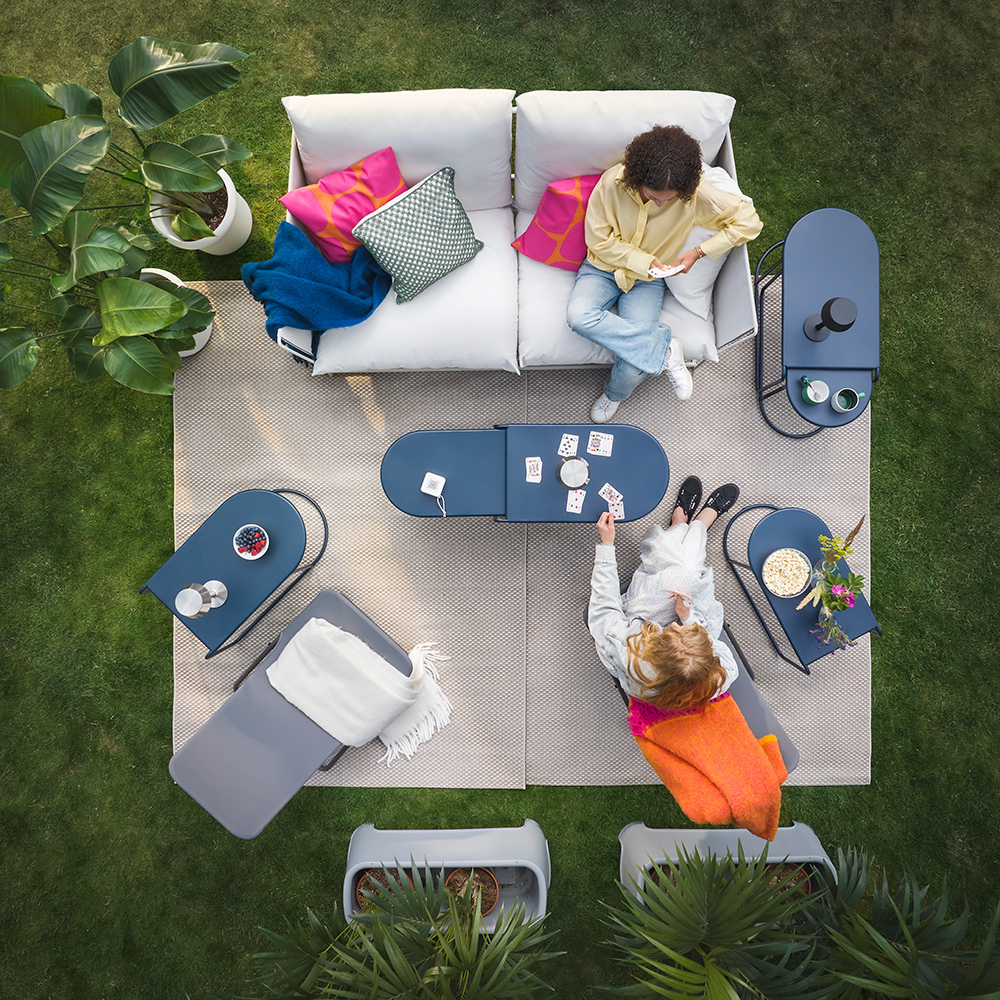 An oudoor lounge area in the garden, with white sofas and bright orange pillows, featuring GRYTSHOLM nest of tables.