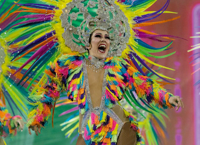 Dancer in a vibrant carnival costume with a silver headdress and colorful feathers, smiling joyfully during a parade. Energetic and bright.