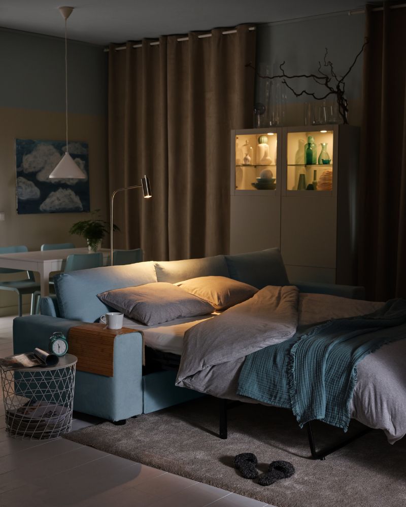 Sala con sofá cama BÅRSLÖV, bandeja RÖDEBY, sábana NATTJASMIN y alfombra STOENSE en un ambiente cálido y acogedor.