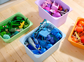Green, purple, blue, and orange storage bins on a wooden floor, each filled with toys sorted by color. Simple and effective organization for kids.