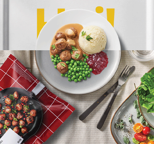 Foto cenital de un plato con albóndigas vegetales, puré, guisantes y mermelada, rodeado por un paquete de HUVUDROLL, cubiertos y una ensalada.