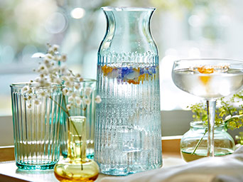 Fluted glass carafe with water and floating flowers, paired with matching glasses and small decorative vases on a bright, clean surface.