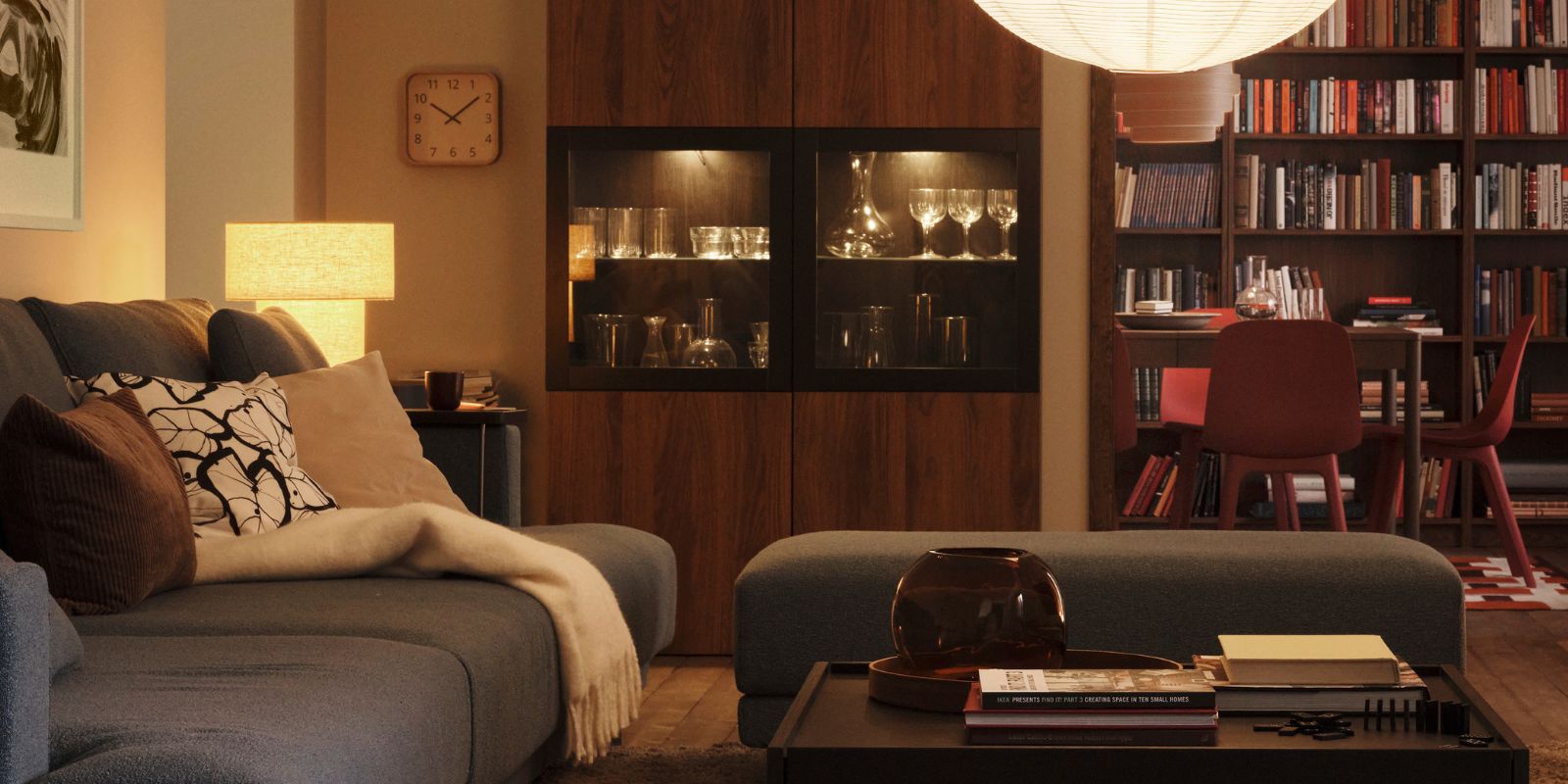 Una lámpara con una pantalla colgante GULLSUDARE cuelga en una sala de estar con una lámpara de mesa STOCKHOLM 2025 en una esquina.