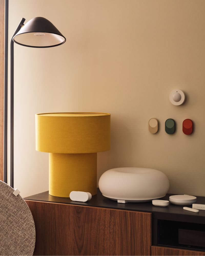 Un sensor de movimiento inalámbrico MYGGSPRAY y tres mandos a distancia BILRESA están montados en una pared sobre un mueble de televisión junto a una lámpara.