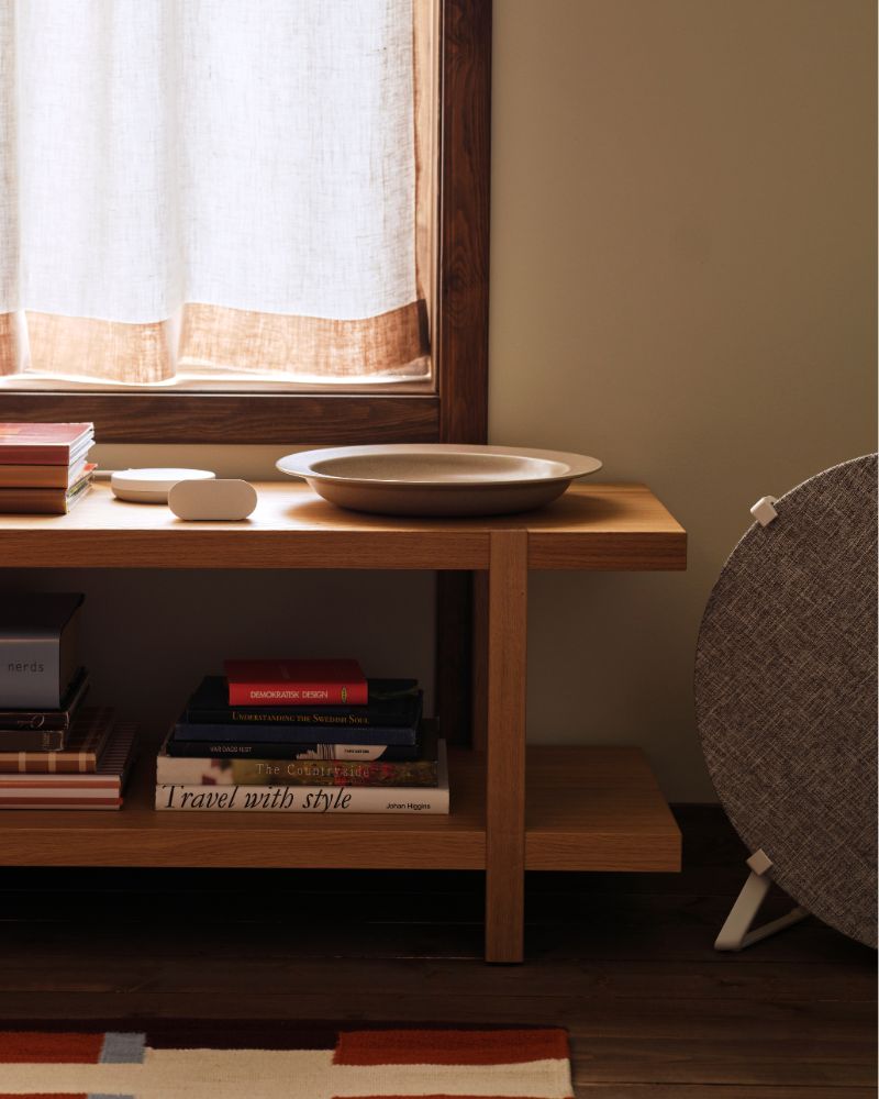 Un sensor de calidad del aire ALPSTUGA se encuentra sobre una estantería/banco STOCKHOLM 2025 situada junto a un purificador de aire STARKVIND.