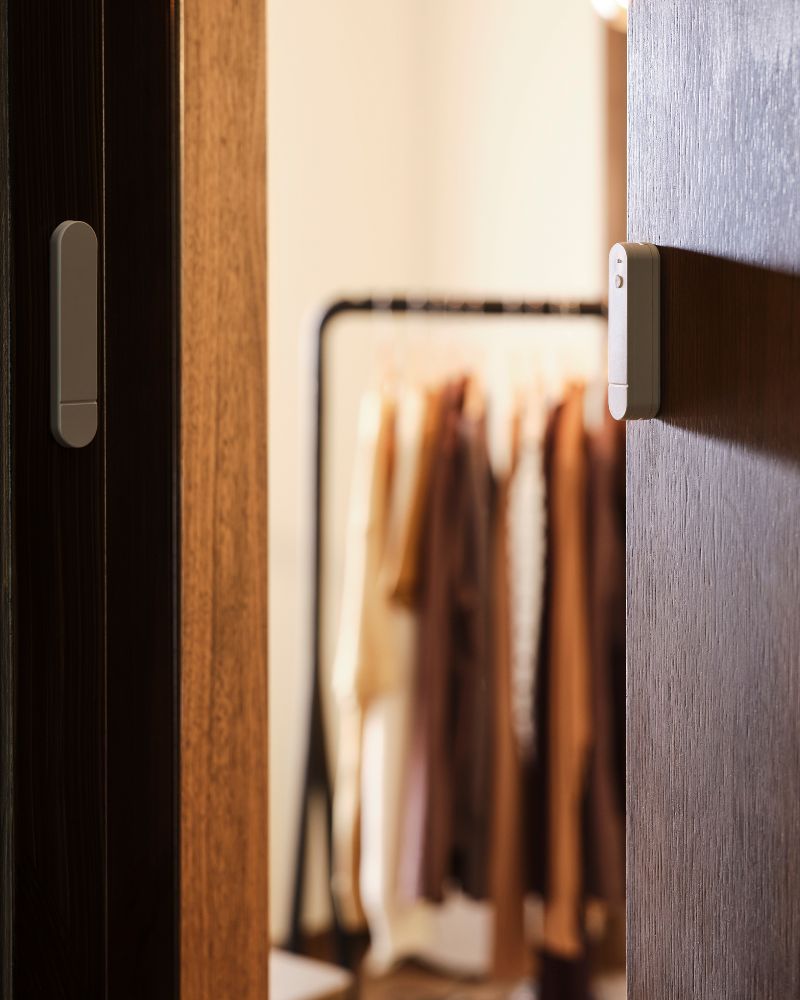 Las dos partes de un sensor de puerta/ventana MYGGBETT se montan en una puerta y en el marco de la puerta. La puerta está abierta.