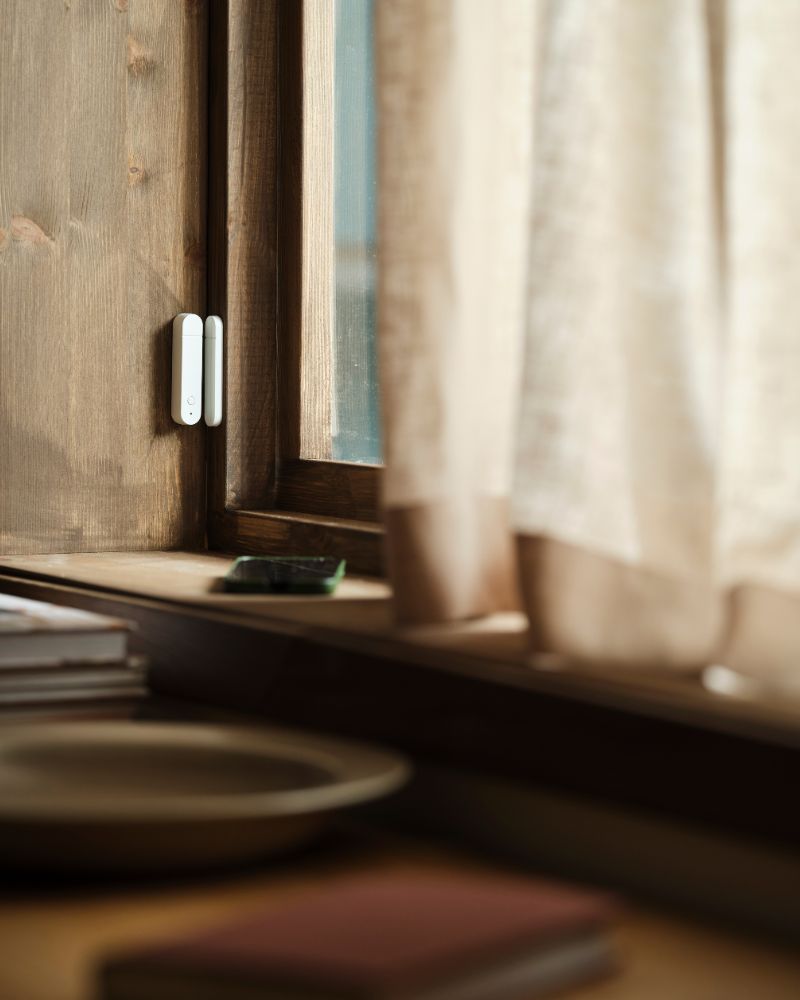  Un sensor de puerta/ventana MYGGBETT se monta en una ventana y en el marco de una ventana. La ventana está cerrada.