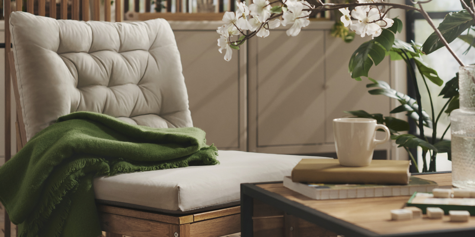 A balcony with greenery features a light brown stained NÄMMARÖ easy chair with light grey-beige cushions and a wooden table.