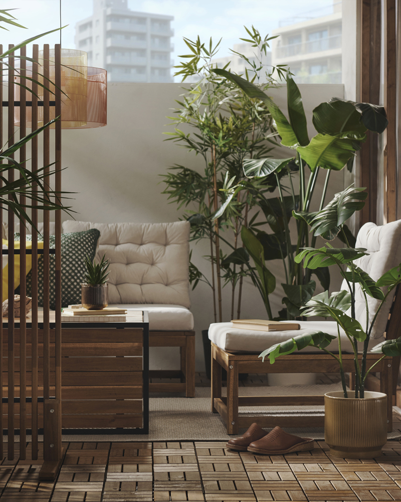 A balcony with light brown stained HÅKANSKÄR coffee table surrounded by plants and outdoor seating, creating a relaxing space.