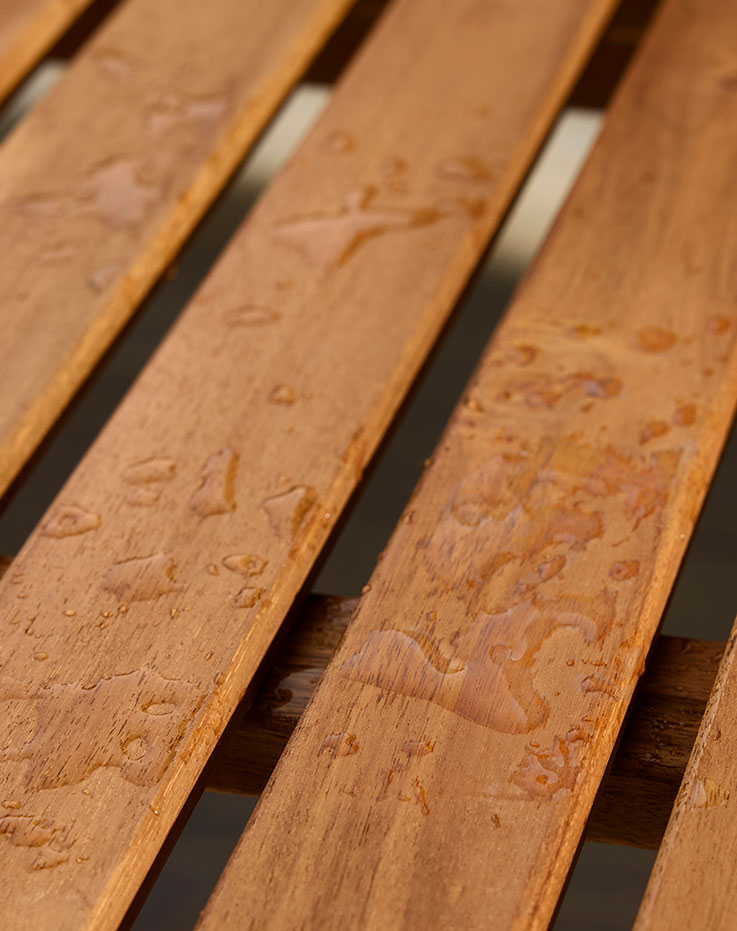 A wooden outdoor table with three brushes next to a can of TRIXIG outdoor wood stain placed on the table.