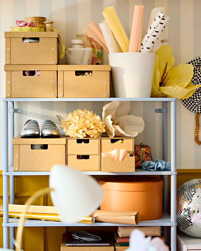 Estantería metálica azul con cajas de cartón, rollos de papel de colores y zapatos plateados. Detalle de decoración creativa y organizada.