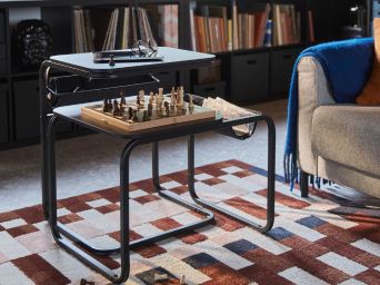 A living room with a chess game on an OLSERÖD side table beside a sofa and on a patterned MARKBLÅMME low pile rug.