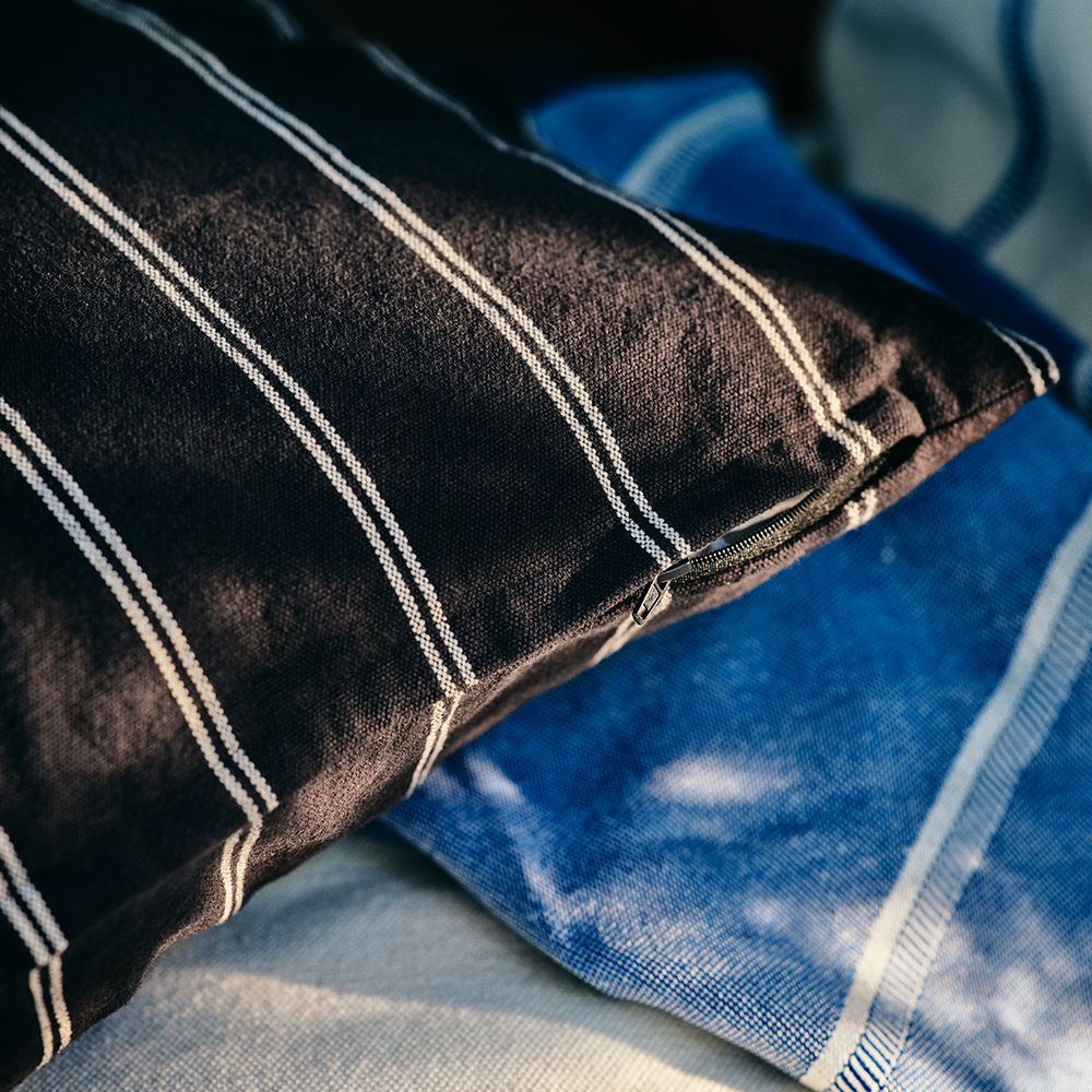 Una funda de cojín SOLUPPGÅNG con rayas blancas y negras está sobre una manta SOLUPPGÅNG.