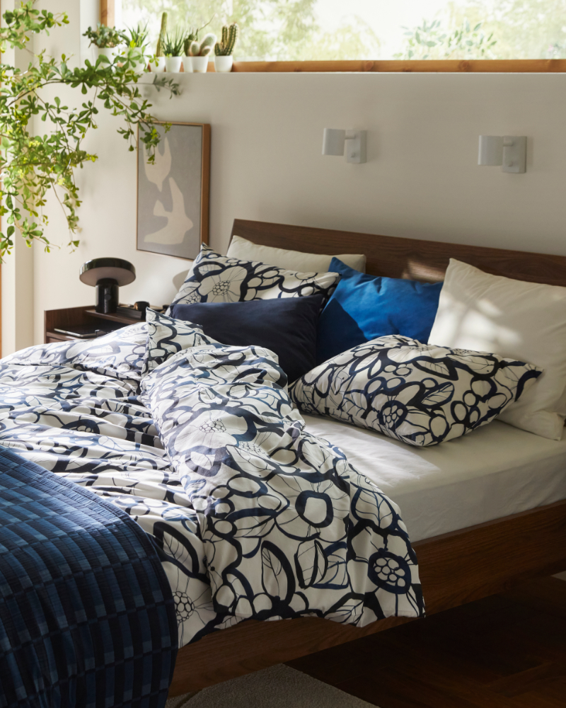 A brown bed frame with white black/blue HÄRLIR duvet cover and pillowcases and a blue SKOGSKOVALL bedspread.