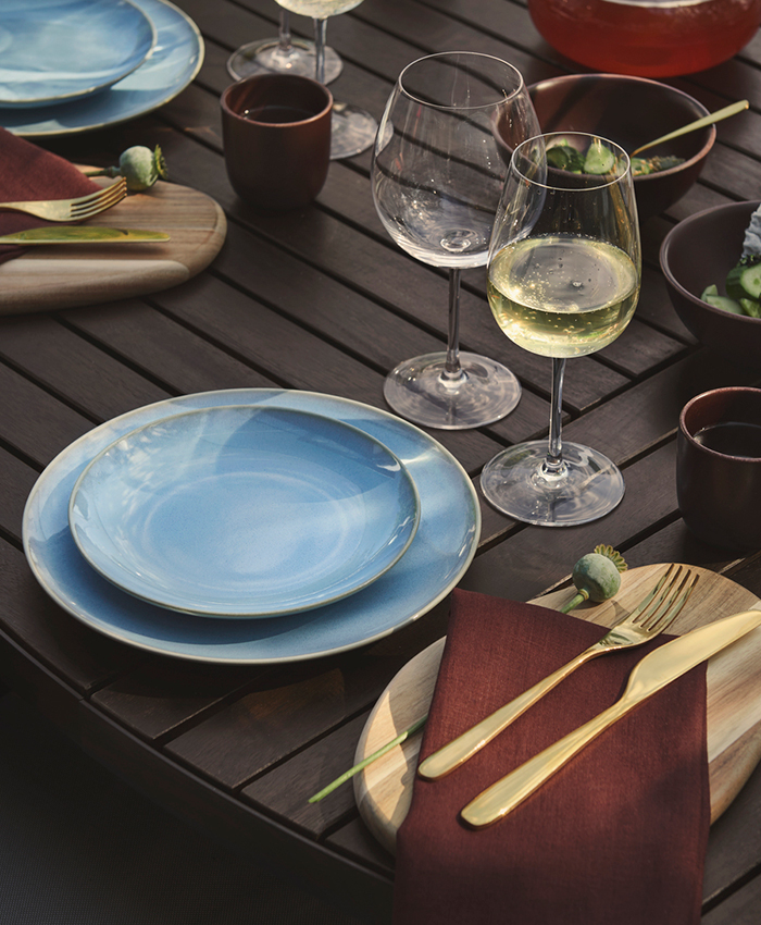 Mesa elegante con vajilla azul, copas de cristal y cubiertos dorados sobre una superficie rústica de madera oscura.