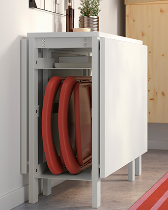 Mesa blanca plegable con sillas rojas guardadas dentro.