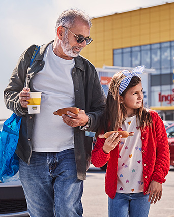 Un hombre y una niña comiendo hot dogs afuera de un IKEA.