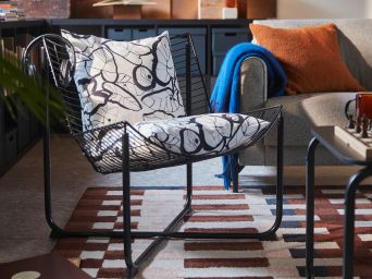A living room features a black SKÅLBODA armchair with two PELARKÖRSBÄR cushion covers, a wooden coffee table, and a soft rug.