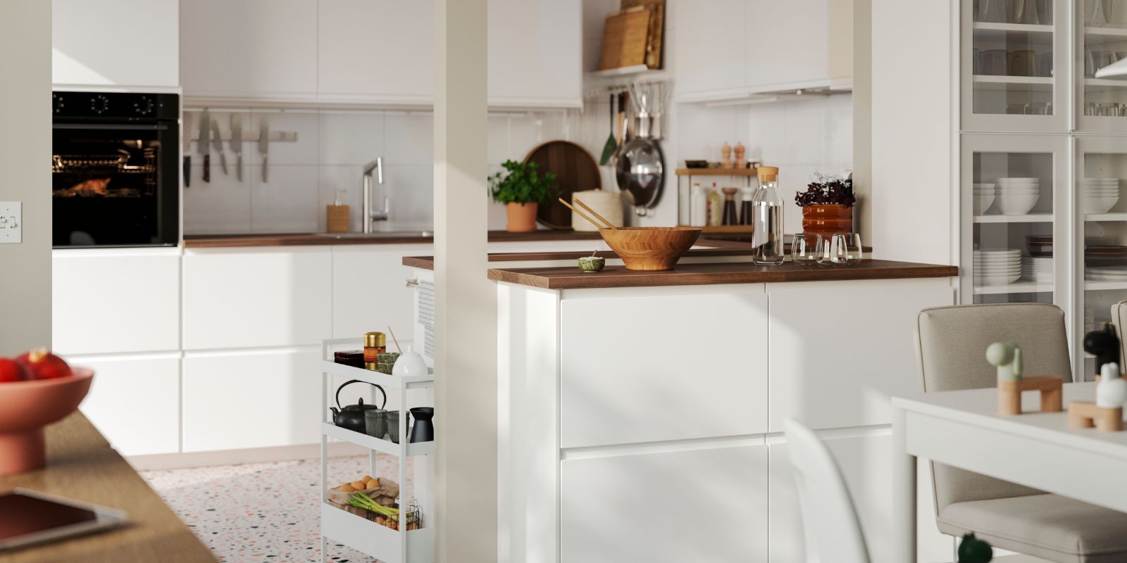 A bright kitchen has matt white VOXTORP fronts and a kitchen peninsula with a white dining table in the foreground.
