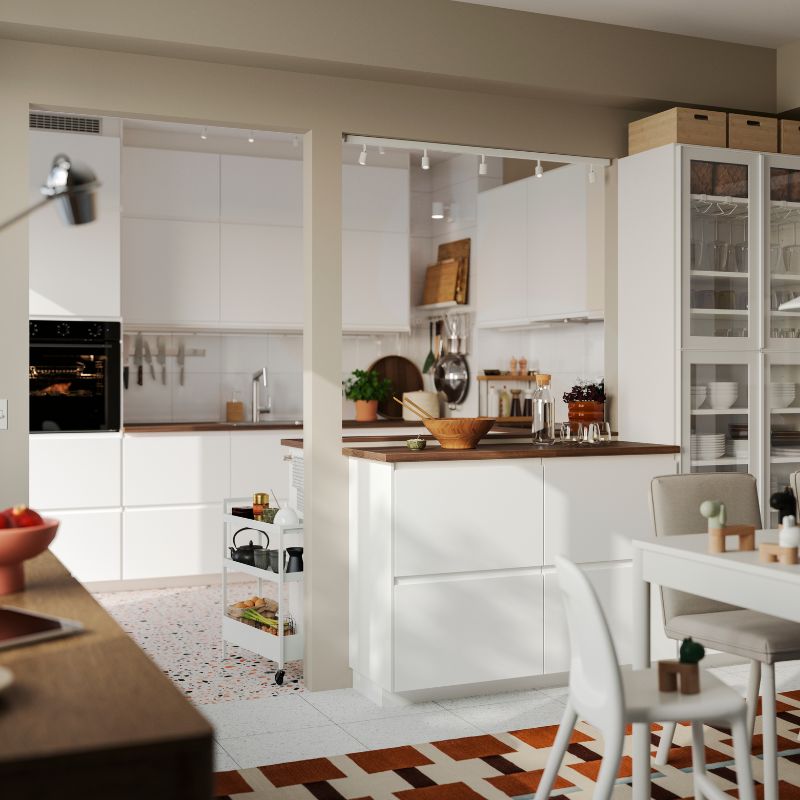 A bright kitchen has matt white VOXTORP fronts and a kitchen peninsula with a white dining table in the foreground.