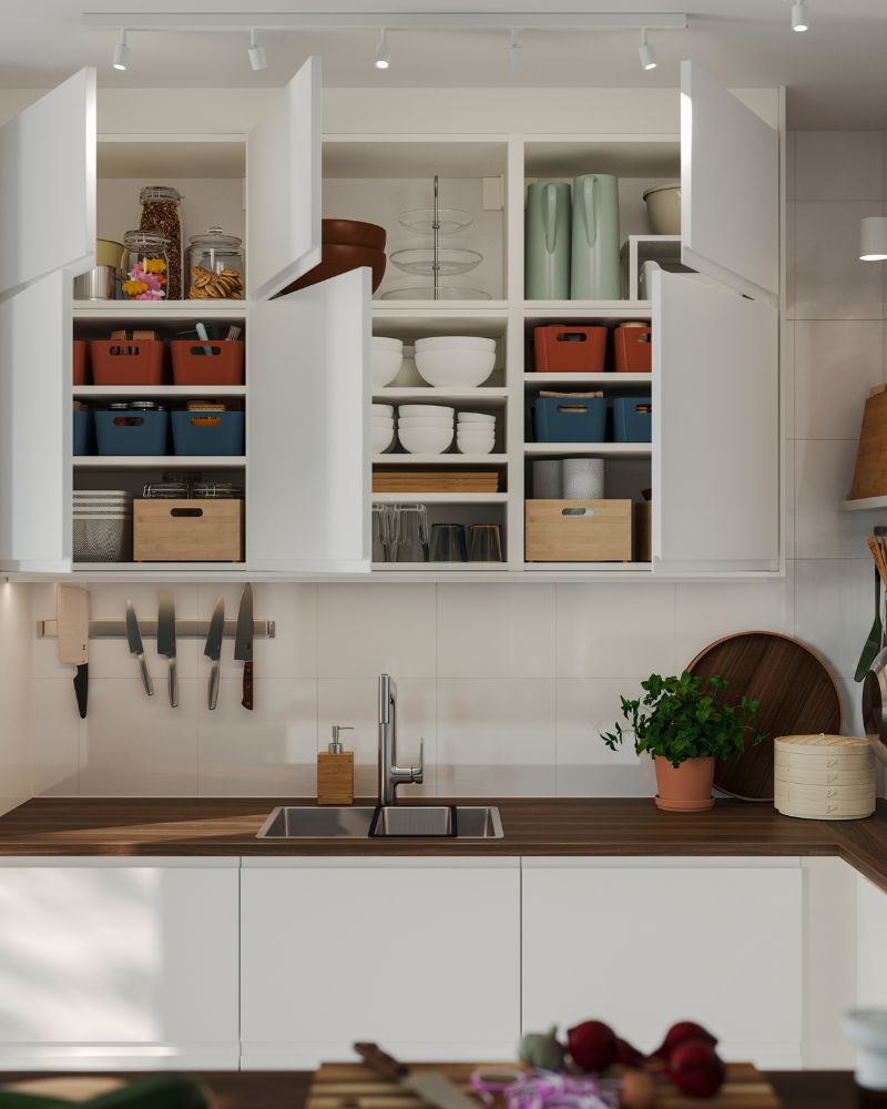 Wall-mounted kitchen cabinets have matt white VOXTORP doors and some of them have been opened, showing items stored inside.