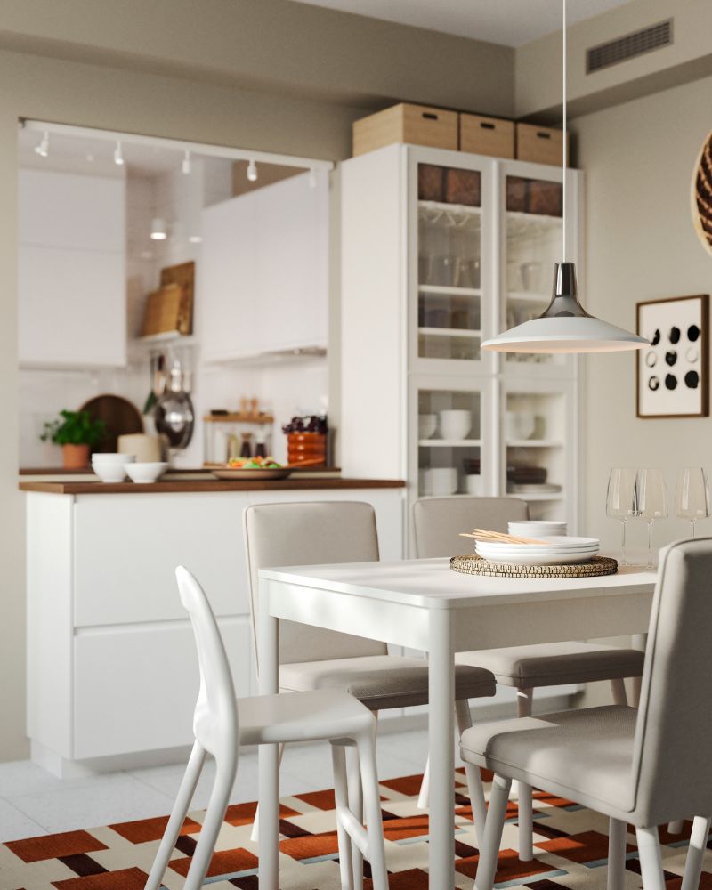 A white kitchen has a peninsula made of METOD kitchen cabinets and there’s a dining table and chairs in white.