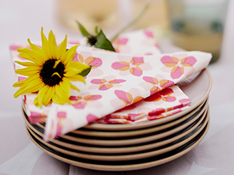 Pila de platos con servilletas florales y un girasol bajo una iluminación suave.