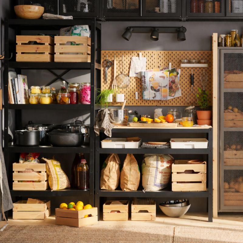 Storage area next to the kitchen with shelves, wooden boxes, hanging utensils on hooks, and recycling bins.