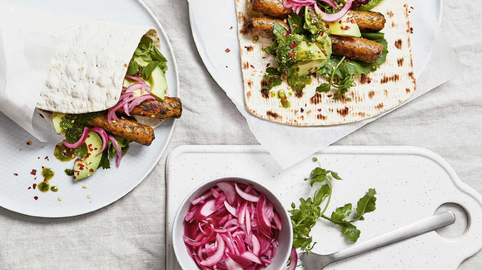 Perros calientes vegetarianos con aguacate, salsa de hierbas, cebolla roja encurtida y hojuelas de chile.