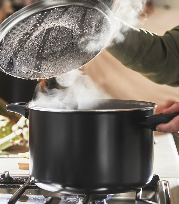 Olla negra sobre el fuego soltando vapor al levantar la tapa de cristal.