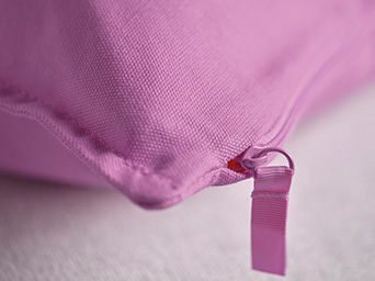 Close-up of a pink cushion with a zipper and thick fabric texture.