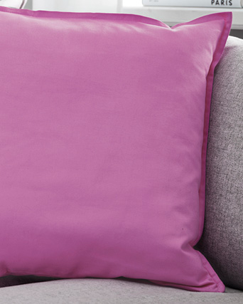 Plain pink cushion with a decorative flange on a light grey sofa.