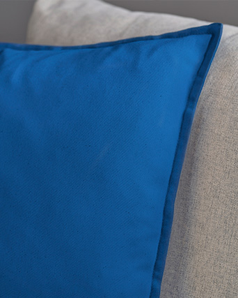Deep blue cushion with a decorative border against a light grey sofa backrest.