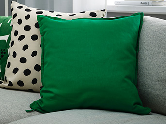 Deep green cushion next to a black-dotted one on a grey sofa.
