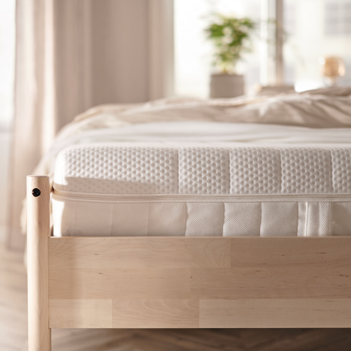White mattress on a wooden bed frame in a bright bedroom with minimalist decor.