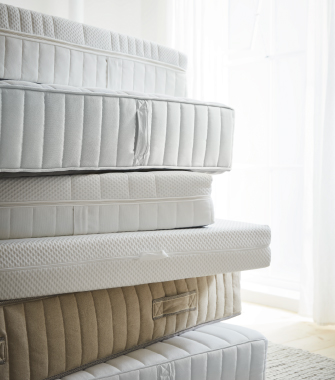 Stacked mattresses in light tones showing different layers and quilted finishes.