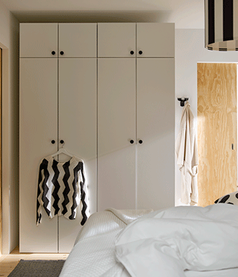 A sun-drenched bedroom with light-coloured walls and a rug, with LASTARE wardrobe combinations. A sweater hangs for the knob.