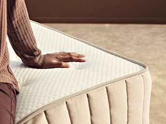 Close-up of a hand resting on the tufted, textured surface of a beige mattress, highlighting its soft comfort and quality.