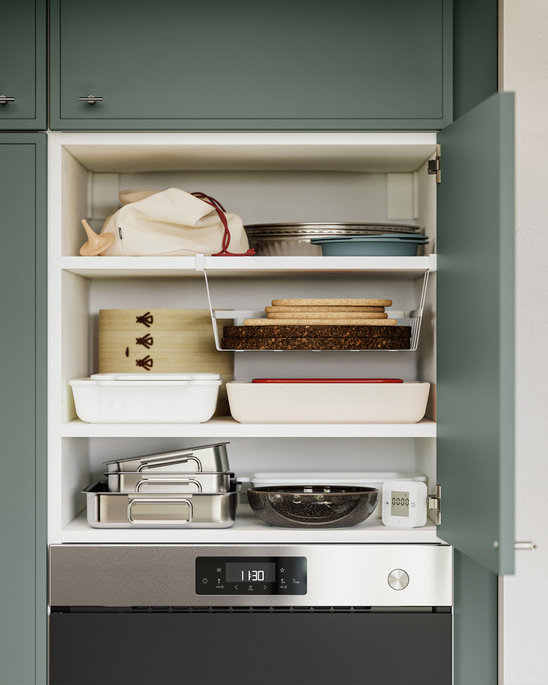 Un armario de cocina tiene la puerta abierta y en los estantes del interior se guardan utensilios de cocina. Uno de los estantes tiene una cesta con clip PÅLYCKE.
