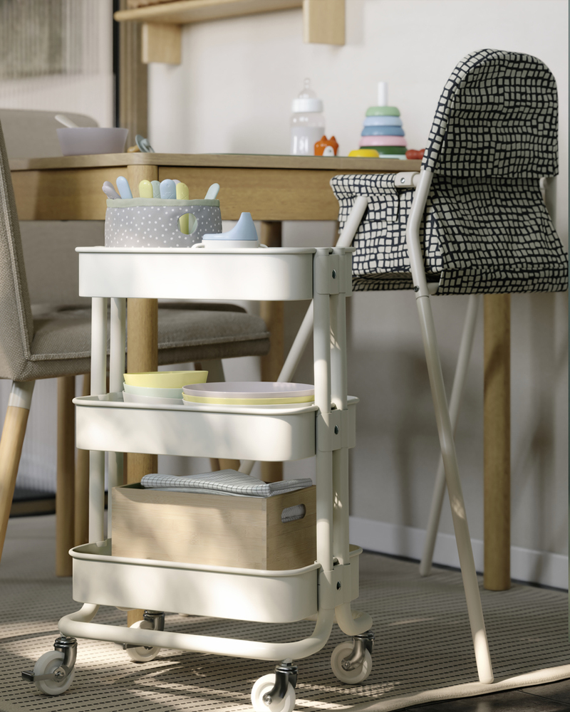 Junto a la mesa extensible TONSTAD hay un carrito RÅSKOG blanco. En sus estantes de malla se guardan artículos para bebés.