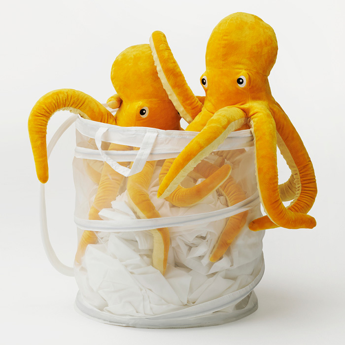 Escena de picnic costero con bolso, manta acolchada y accesorios sobre rocas frente al mar.