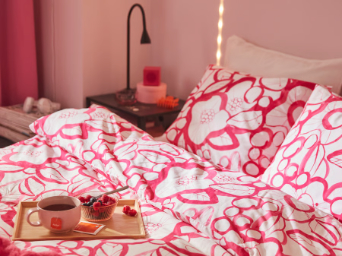 Una cama con una funda nórdica y una funda de almohada HÄRLIR con estampado floral en blanco y rosa intenso, y una colcha GULLSTRÅLE en rosa intenso.
