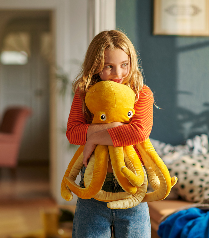 Niña sonríe mientras abraza un peluche amarillo con forma de pulpo
