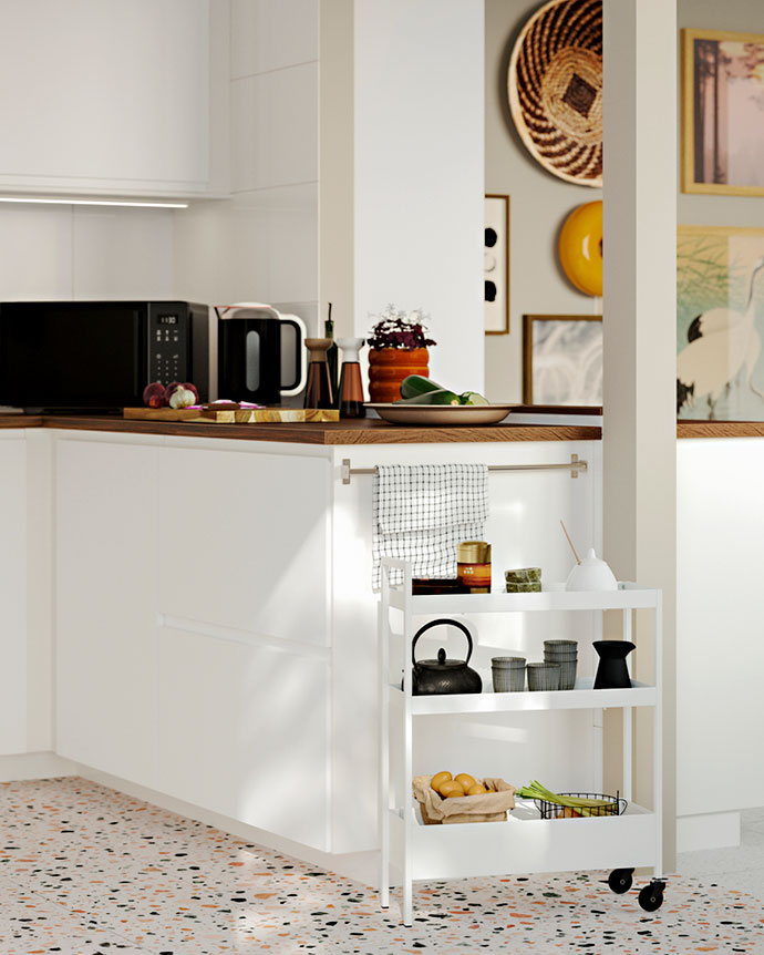 Carrito de cocina blanco con tres estantes junto a una encimera de madera y armarios blancos en una cocina luminosa con suelo de terrazo.